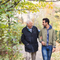An older man and his male companion laugh as they walk through the countryside