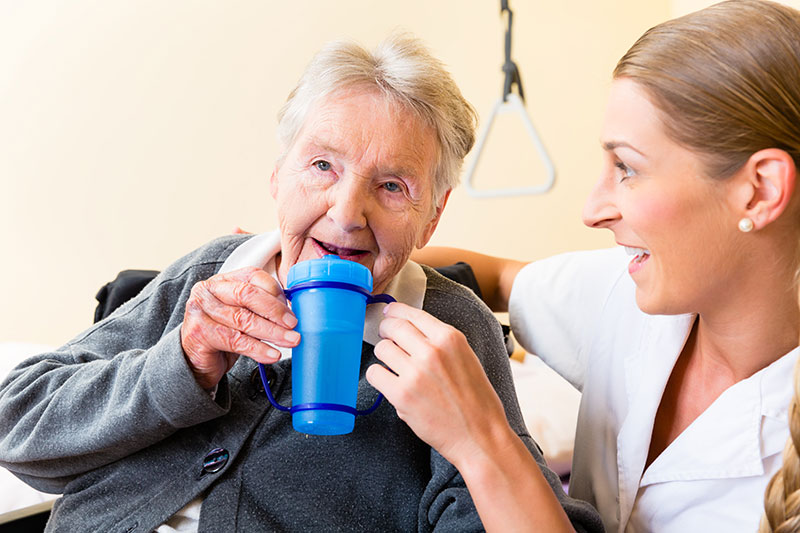 Care worker helps older woman drink from cup