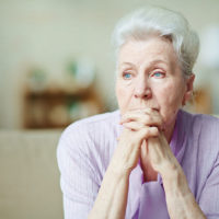 A senior lady rests her head on folded hands