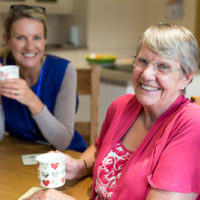 Older lady and care worker smile over tea
