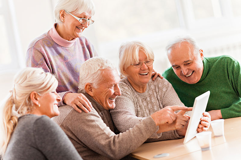 Five seniors gather around a table using a tablet device