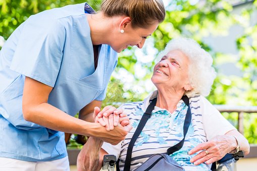 Nurse and senior woman hold hands in care home