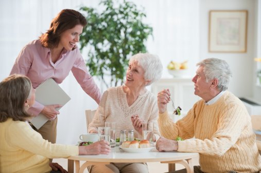 Three seniors and a care worker talk over dinner
